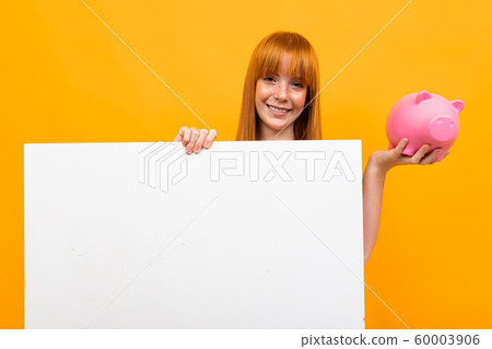 smiling girl holding a piggy bank and a banner in hands over yellow background 60003906