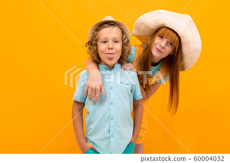 Red-haired girl in a summer hat peeks out from behind a boy on a yellow background Red-haired girl in a summer hat peeks out from behind a boy on a yellow background 60004032