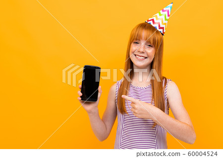 joyful european red-haired girl shows the phone screen over yellow background 60004524