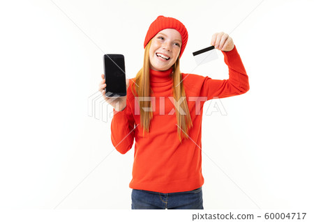 joyful girl looks shows the phone screen and holds a credit card on a white background joyful girl looks shows the phone screen and holds a credit card on a white background 60004717