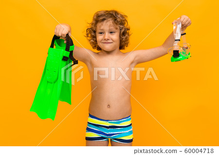 Red-haired curly boy holds swimming flippers on a yellow background Red-haired curly boy holds swimming flippers on a yellow background 60004718