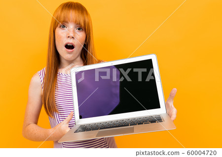 Surprised red-haired girl shows a laptop screen isolated on a yellow background Surprised red-haired girl shows a laptop screen isolated on a yellow background 60004720