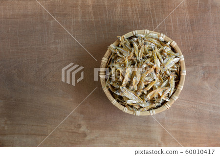top view of raw dried little fish in a bamboo basket on wooden table. 60010417