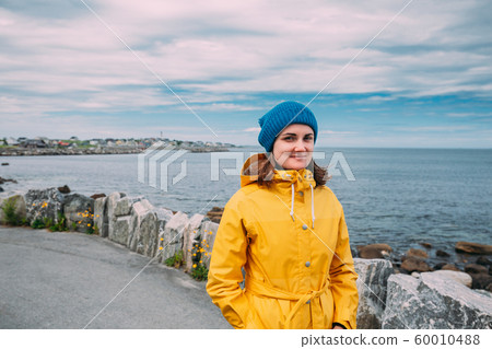 Alnesgard, Godoya, Norway. Portrait Of Young Woman Lady Tourist Traveler In Summer Day In Godoy Island Near Alesund Town Alnesgard, Godoya, Norway. Portrait Of Young Woman Lady Tourist Traveler In Summer Day In Godoy Island Near Alesund Town 60010488