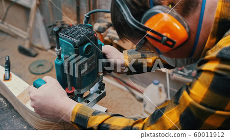 Carpentry indoors - a woodworker polishes the wooden detail from the top in the workshop- a man 60011912