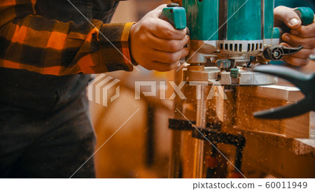 Carpentry indoors - a man woodworker polishes and cutting off the side of a wooden detail 60011949