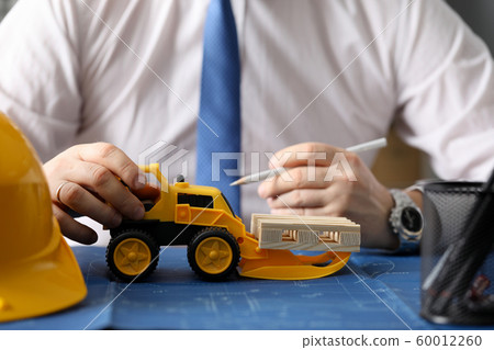 Male constructor hand hold yellow tractor against Male constructor hand hold yellow tractor against 60012260