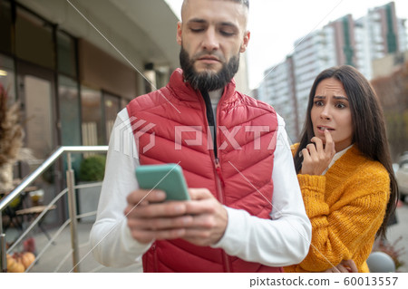 Nervous young woman standing behind her boyfriend Nervous young woman standing behind her boyfriend 60013557