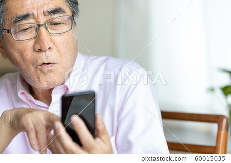 Surprised senior man looking at smartphone 60015035