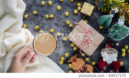 hand holding a cup of hot coffee in winter season with Christmas background decorations and gift boxes on table 60017170
