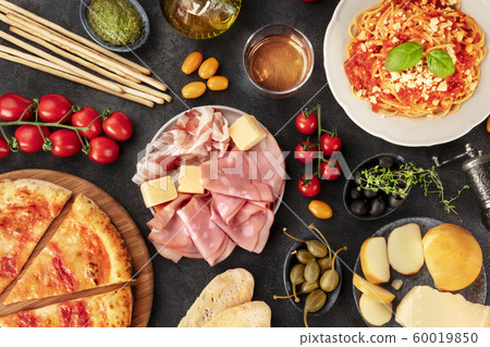 Italian food. Pizza, pasta, cheese, ham, wine, olives, pesto, olive oil, capers, shot from above with a place for text, a flat lay on a dark background Italian food. Pizza, pasta, cheese, ham, wine, olives, pesto, olive oil, capers, shot from above with a place for text, a flat lay on a dark background 60019850
