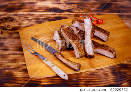 Meat pork ribs on a barbecue grill in the board on tomatoes on a wooden background flat lay. Meat pork ribs on a barbecue grill in the board on tomatoes on a wooden background flat lay. 60020762