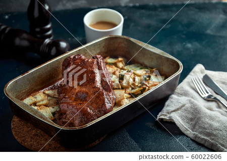 Roasted pork neck with baked potatoes and herbs on a tray on the black background Roasted pork neck with baked potatoes and herbs on a tray on the black background 60022606