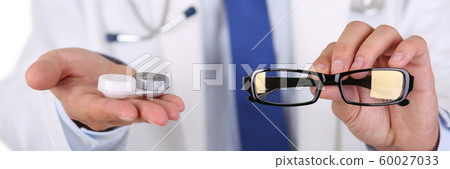 Male doctor hands giving pair of black glasses and contact lens 60027033