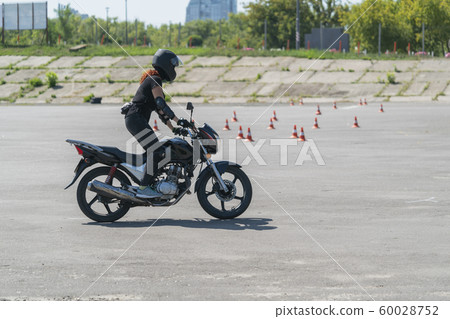 Girl with red hair and in dome learning to ride a bike at motorcycle racing track. Biker on a motorcycle. 60028752