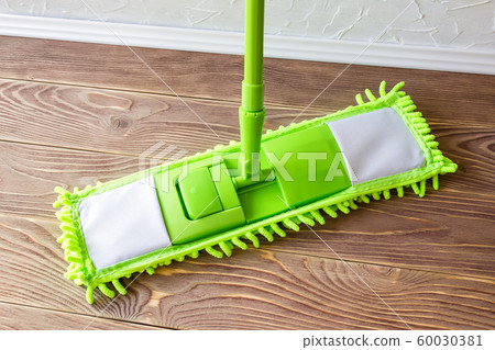 Green plastic mop on a brown wooden floor. Wash the floor. Housekeeping and household chores. 60030381