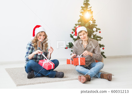 Holidays, christmas and family concept - Young happy couple opening gifts at home. 60031213