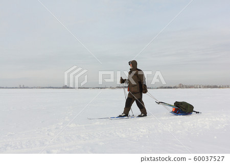 Man skiing with sleigh a frozen river in winter Man skiing with sleigh a frozen river in winter 60037527