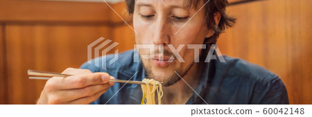 Male tourist eating Korean noodles in a Korean cafe. Travel Korea Concept BANNER, LONG FORMAT 60042148