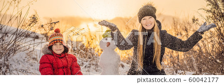 Happy family in warm clothing. Smiling mother and son making a snowman outdoor. The concept of Happy family in warm clothing. Smiling mother and son making a snowman outdoor. The concept of 60042177