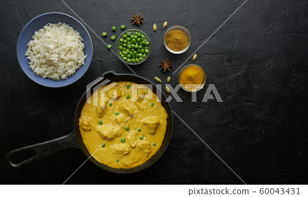 Cooking tasty butter chicken curry dish with rice in a cast iron pan 60043431