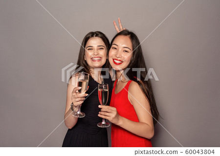 Freestyle. Young girls in dresses standing isolated on gray with glasses of champagne posing to 60043804