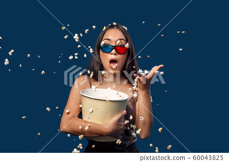 Freestyle. Young woman in 3d glasses standing isolated on dark blue throwing popcorn aside shocked 60043825