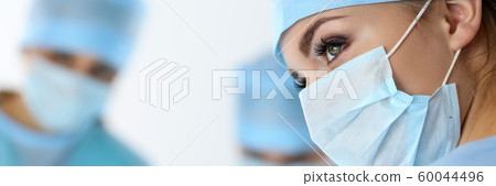 Three surgeons at work operating in surgical theatre saving patient 60044496