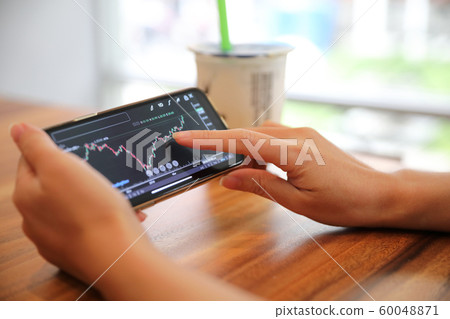 Female hand with smartphone trading stock online in coffee shop , Business concept 60048871