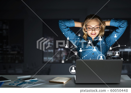 Attractive blonde wearing glasses in dark office using laptop. Mixed media 60050448