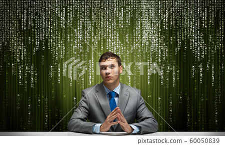 Young serious man folded hands and sitting at desk Young serious man folded hands and sitting at desk 60050839