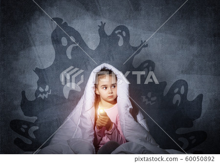 Scared girl with flashlight under blanket Scared girl with flashlight under blanket 60050892