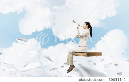 Young woman playing trumpet and sitting on book Young woman playing trumpet and sitting on book 60051141
