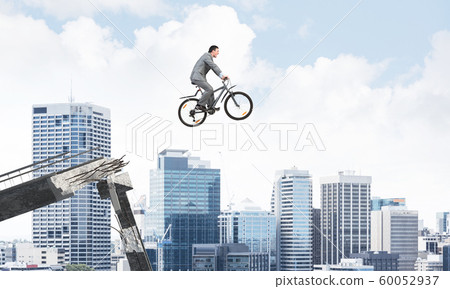 Businessman on bike jumping from broken bridge Businessman on bike jumping from broken bridge 60052937