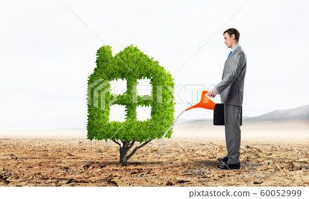 Businessman watering green plant in shape of house Businessman watering green plant in shape of house 60052999
