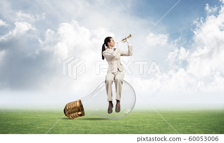 Woman sitting on light bulb and playing trumpet 60053006