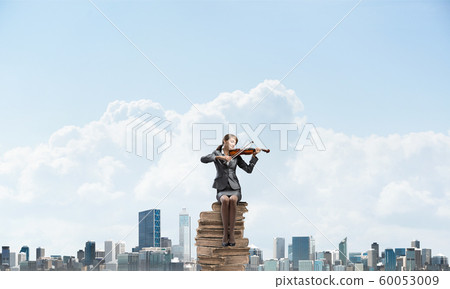 Young woman with violin sitting on stack of books Young woman with violin sitting on stack of books 60053009