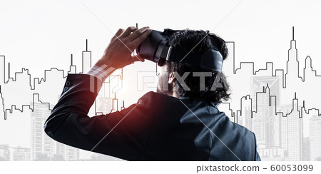 Handsome businessman against sunrise above city experiencing impressive virtual reality 60053099