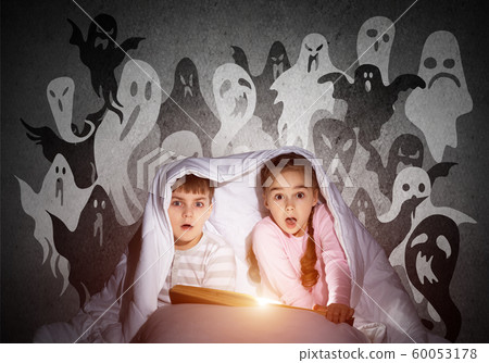 Scared girl and boy reading book in bed 60053178