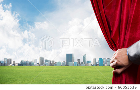 Green meadow behind red curtain and hand holding it Green meadow behind red curtain and hand holding it 60053539