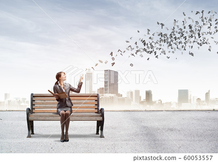 Young woman holding open book on wooden bench Young woman holding open book on wooden bench 60053557