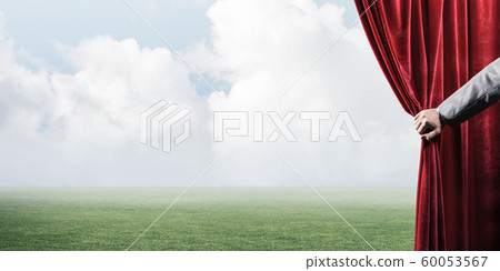 Green meadow behind red curtain and hand holding it Green meadow behind red curtain and hand holding it 60053567