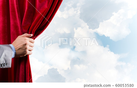 Cloudy landscape behind red curtain and hand holding it Cloudy landscape behind red curtain and hand holding it 60053580