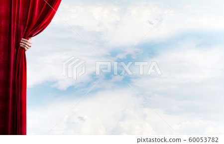 Cloudy landscape behind red curtain and hand holding it 60053782