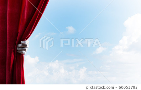 Cloudy landscape behind red curtain and hand holding it Cloudy landscape behind red curtain and hand holding it 60053792