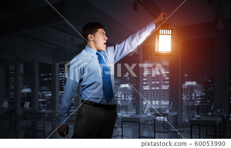 Scared businessman holding glowing lantern Scared businessman holding glowing lantern 60053990