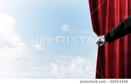 Cloudy landscape behind red curtain and hand holding it 60054498