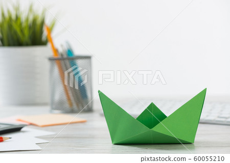 Wooden office desk with green origami boat. 60055210