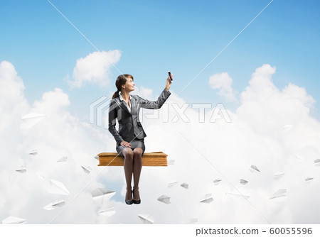 Attractive girl sitting on book and flying in sky 60055596