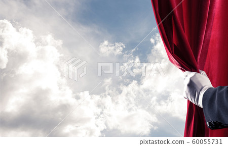 Cloudy landscape behind red curtain and hand holding it Cloudy landscape behind red curtain and hand holding it 60055731